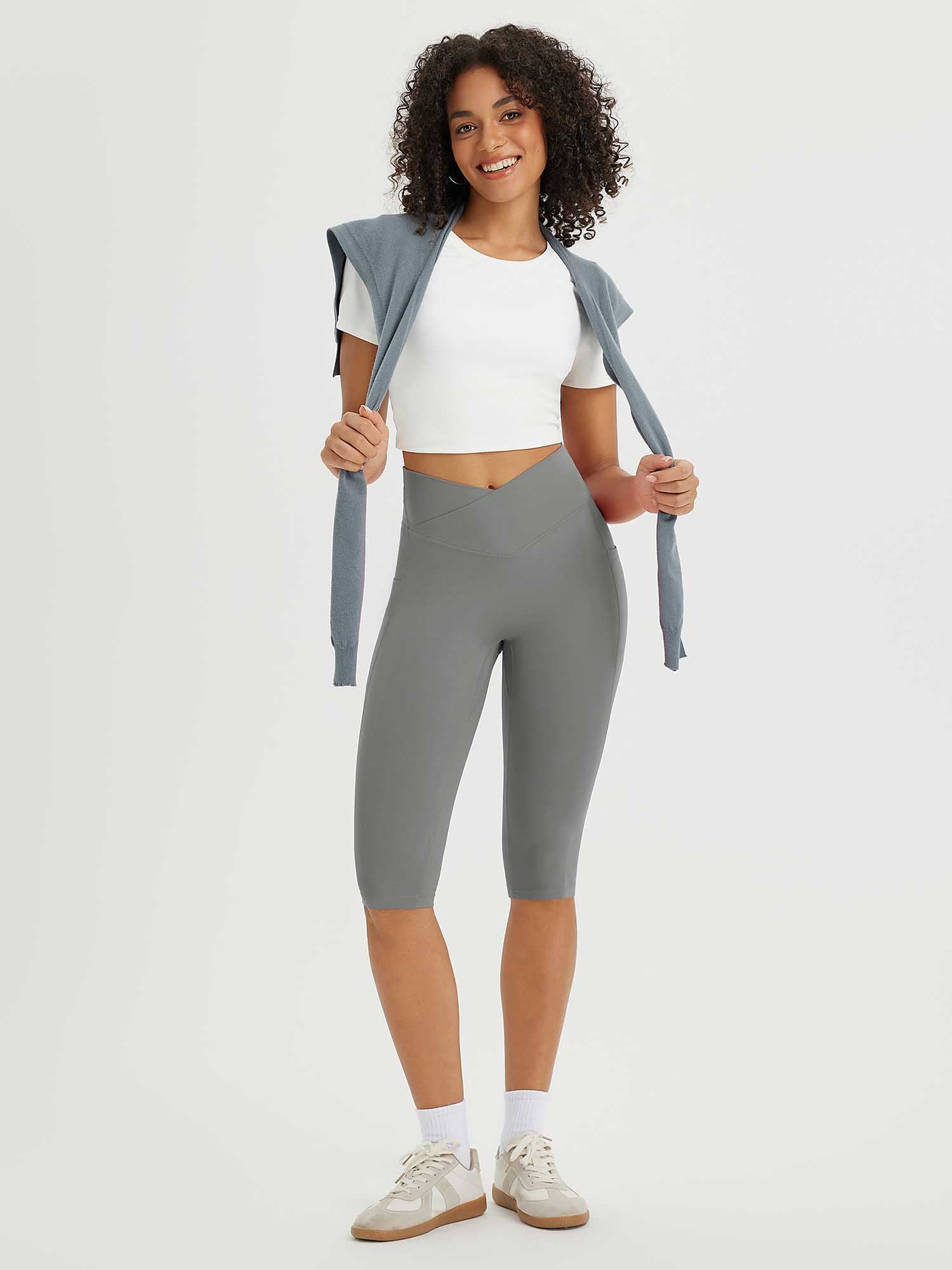 Woman in grey 14" high-waisted crossover capris and white crop top, smiling with a sweater over shoulders. #color_Dark Gray
