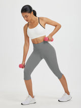 Woman in gray 17" high-waisted capris and white sports bra lifting pink dumbbells. #color_Dark Gray