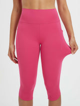 Woman stretching hot pink high-waisted 17-inch capri leggings with side pockets. #color_Rose Red