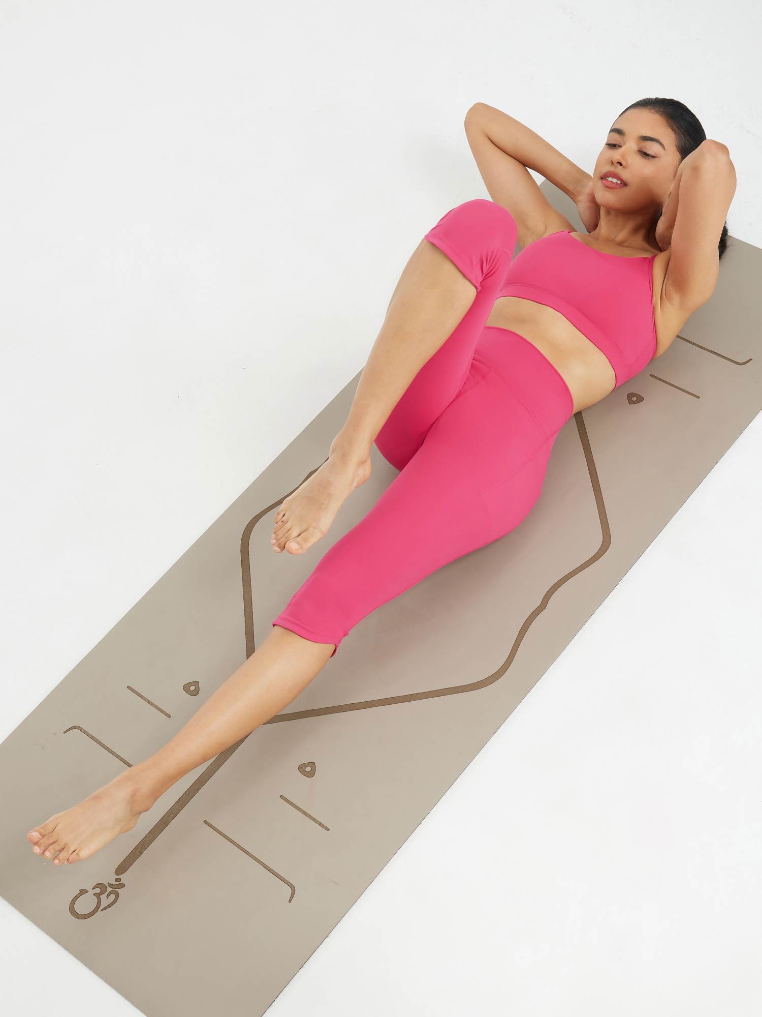Woman in pink high-waisted capris and sports bra doing bicycle crunches on a yoga mat with Om symbol. #color_Rose Red