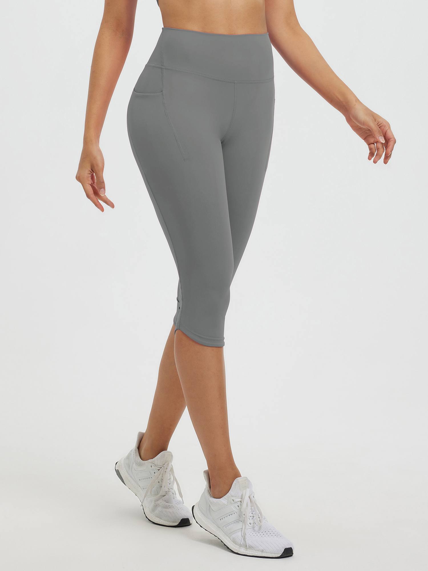 Women's grey 17" high-waisted capri leggings with side pockets and white athletic shoes. #color_Dark Gray