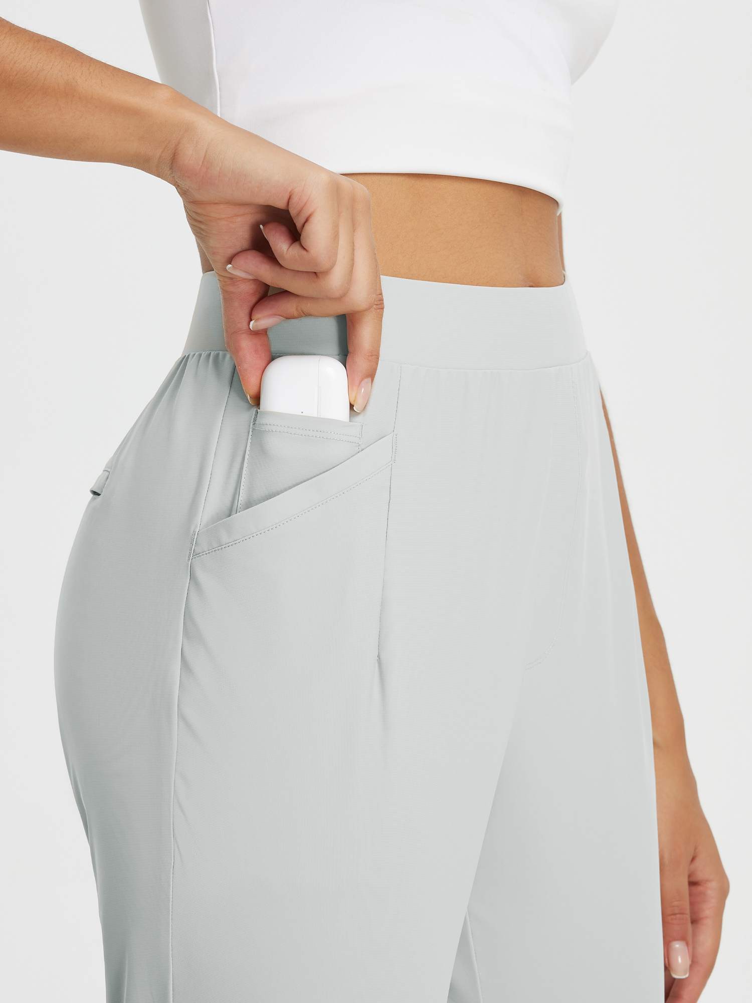 Hand placing earbuds in pocket of light grey high-rise tapered trousers for outdoor travel. #color_Light Gray