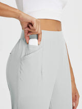 Hand placing earbuds in pocket of light grey high-rise tapered trousers for outdoor travel. #color_Light Gray