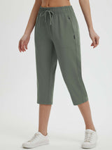 Women's olive green 19" quick-dry yoga capri pants with drawstring and pockets, paired with white sneakers. #color_Army Green