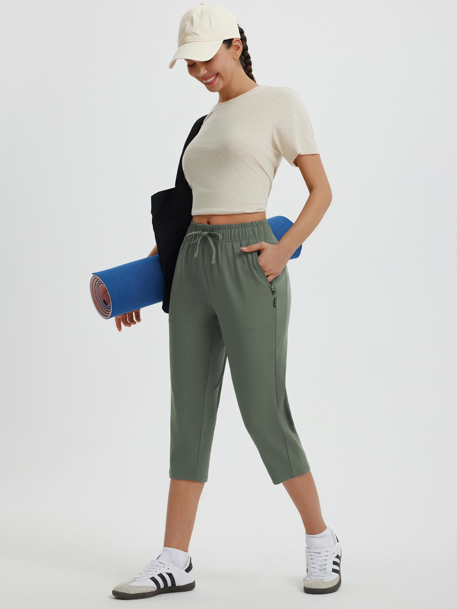 Olive green women's 19" quick-dry yoga capri pants with drawstring and zip pockets, holding yoga mat.