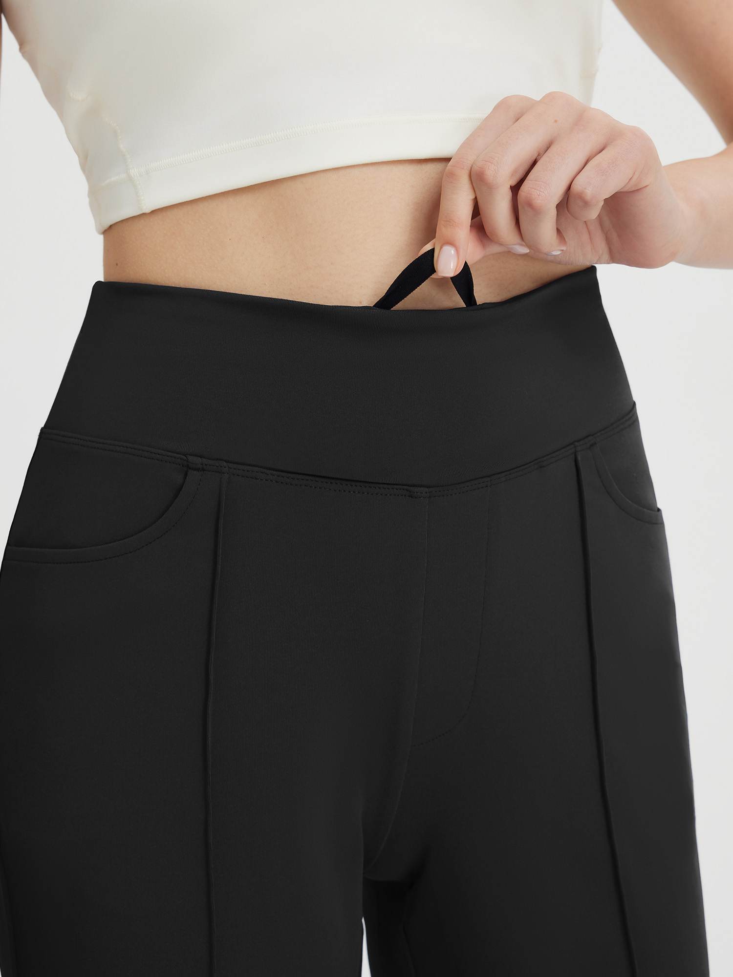 Close-up of black women's high-waisted capris with a hand reaching for the internal drawstring. #color_Black