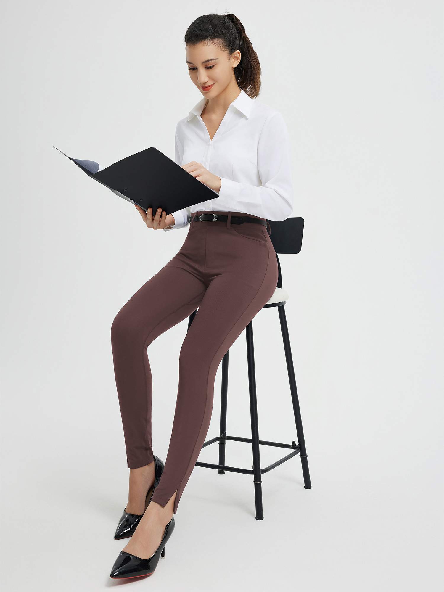 Woman in brown high-waisted tight business yoga pants with split hem, holding folder. #color_Dark Brown