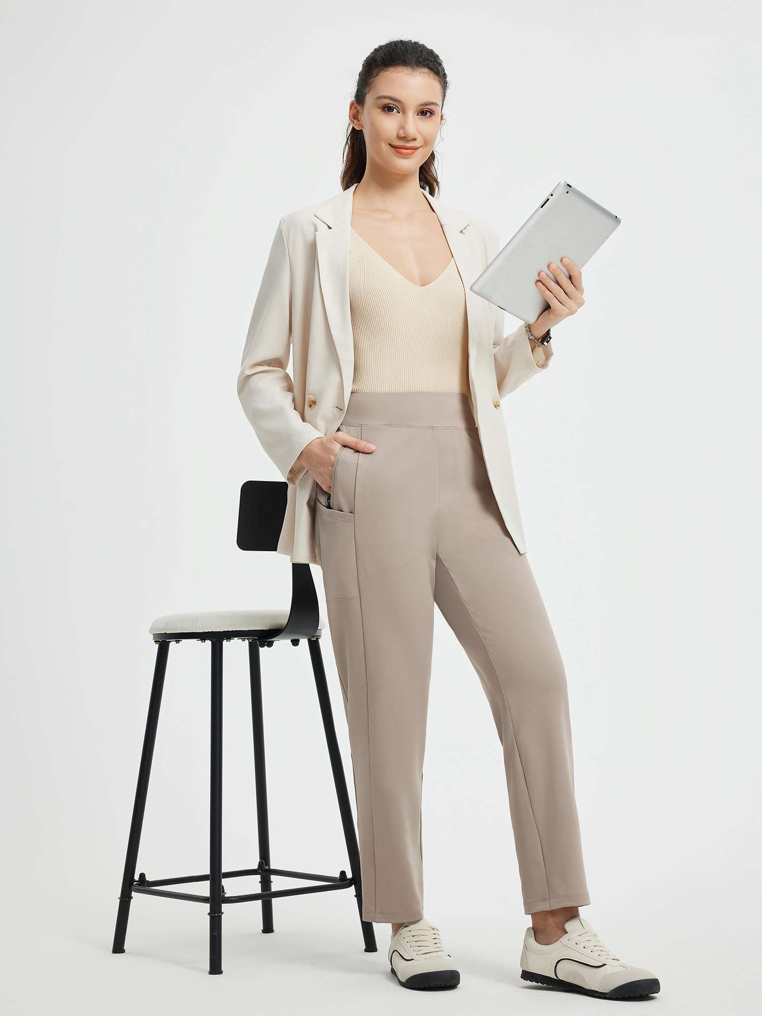 Model wearing taupe yoga tapered pants, beige blazer, holding tablet. #color_Teak Brown