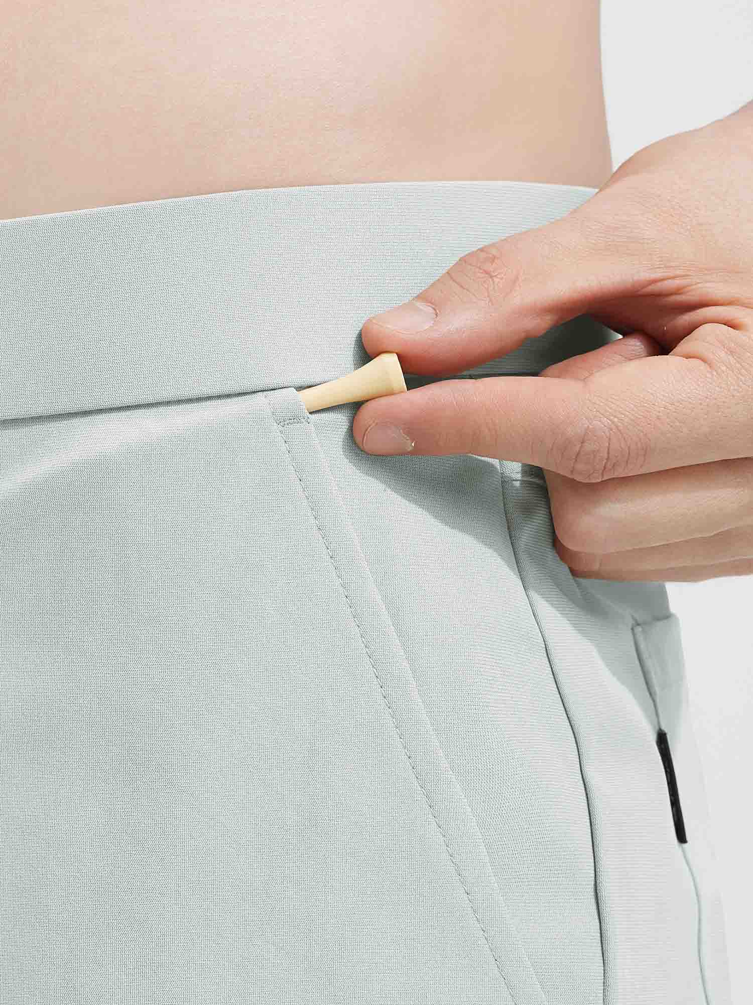 Baleaf light green 7" golf shorts, hand placing golf tee in waistband detail. #color_Light Gray