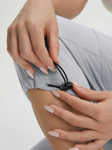 Hands adjusting ankle drawstring on 19-inch Baleaf lightweight cargo capri pants. #color_Light Gray