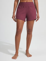 Woman wearing deep red Baleaf 7'' UPF 50+ high-rise board shorts with zipper pockets.