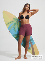 Baleaf maroon 7'' UPF 50+ high-rise board shorts with zipper pockets, holding surfboard.