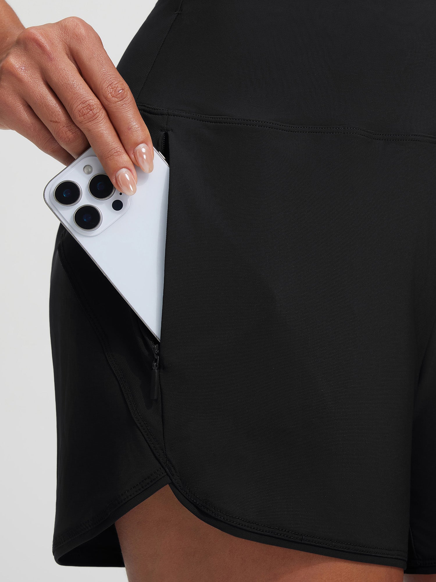 Baleaf black high-rise board shorts with zippered pocket holding smartphone.