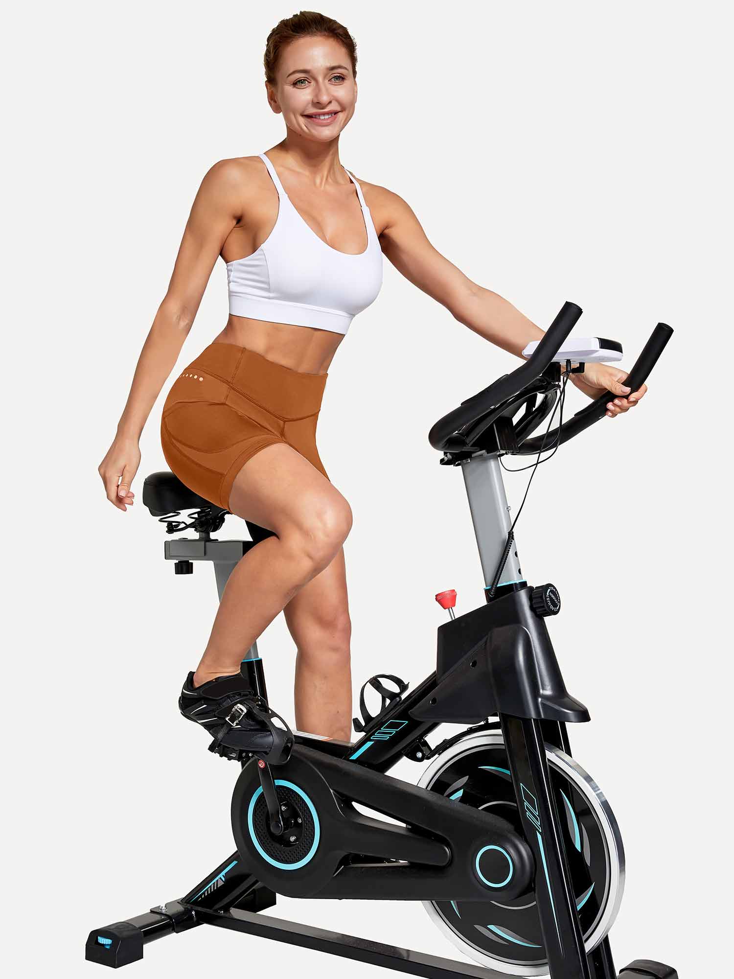 Women's brown V-waist cycling shorts with tummy control & pockets, model on spin bike. #color_Brown