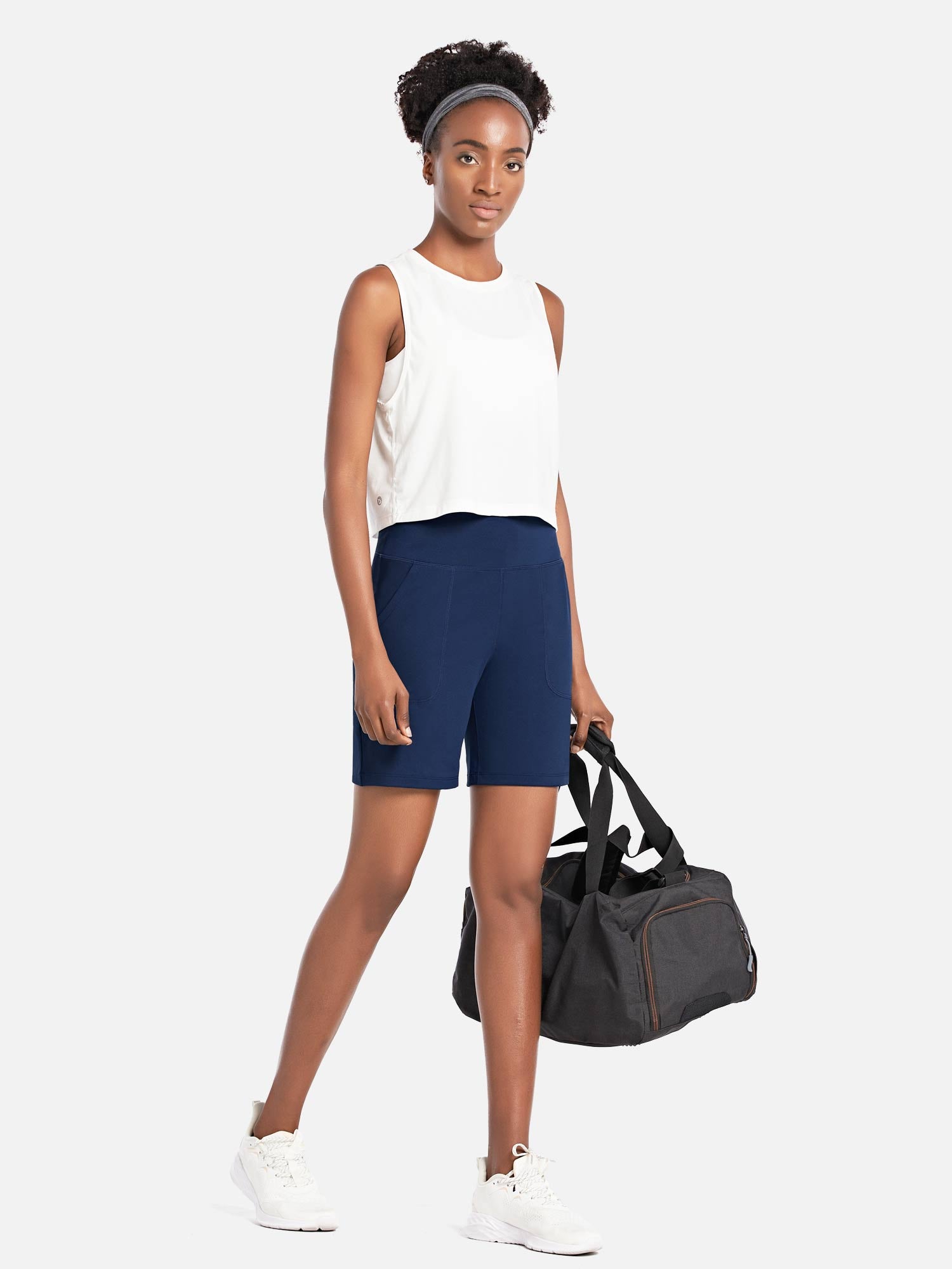 Woman in navy blue Laureate 3-Pocket Athletic Shorts and white tank top holding a duffel bag. #color_Estate Blue