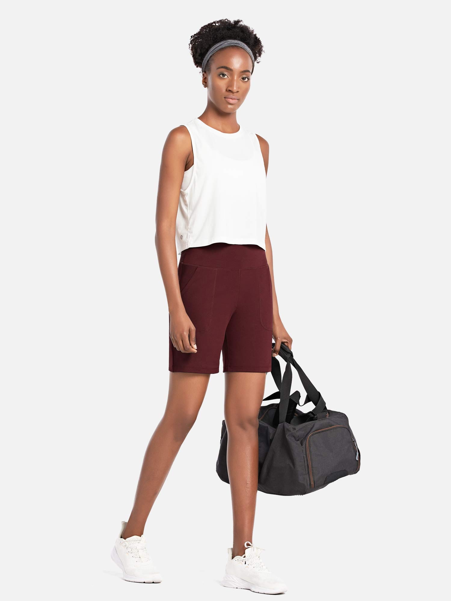 Woman in maroon Laureate 3-Pocket Athletic Shorts and white top, holding a duffel bag. #color_Chocolate Truffle