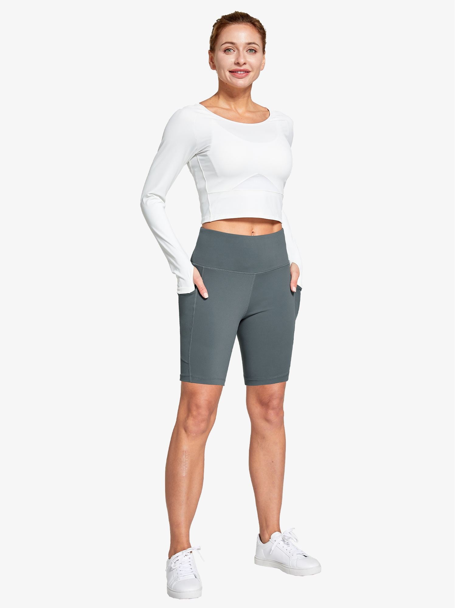 Women's grey high-waisted biker shorts featuring deep pockets, shown on a model with a white long-sleeve top.