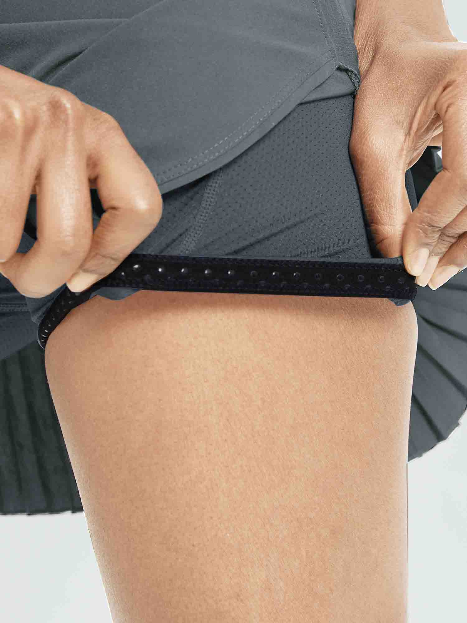 Women's high-waisted running skirt detail: hands revealing anti-slip silicone leg grippers.