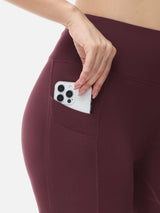 Close-up of burgundy fleece-lined running leggings with a hand placing a phone in a utility pocket. #color_Wine Red