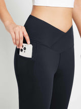 Black crossover waist yoga flare pants with pocket holding phone. #color_Black