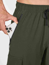 Man placing iPhone in zippered pocket of dark green cargo hiking pants #color_Army Green