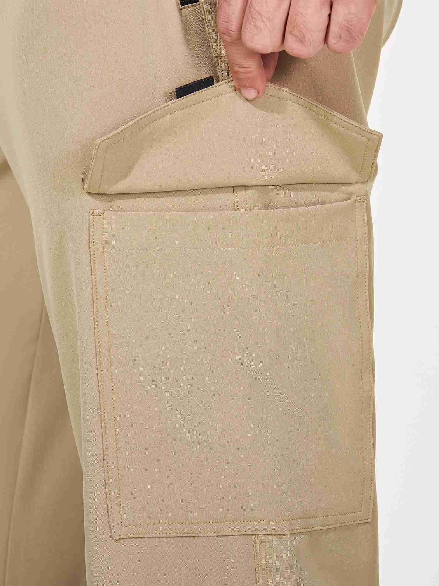 Close-up of men's khaki cargo hiking pants showing a large side pocket and a hand reaching into it. #color_Brown