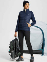 Women's navy quilted outdoor jacket with stretch sleeves, holding backpack near tent. #color_Navy Blue