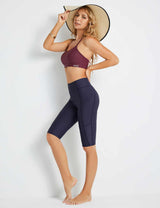 Woman wearing navy Baleaf UPF50+ high-rise swim shorts and a maroon sports bra, holding a wide-brimmed straw hat.
